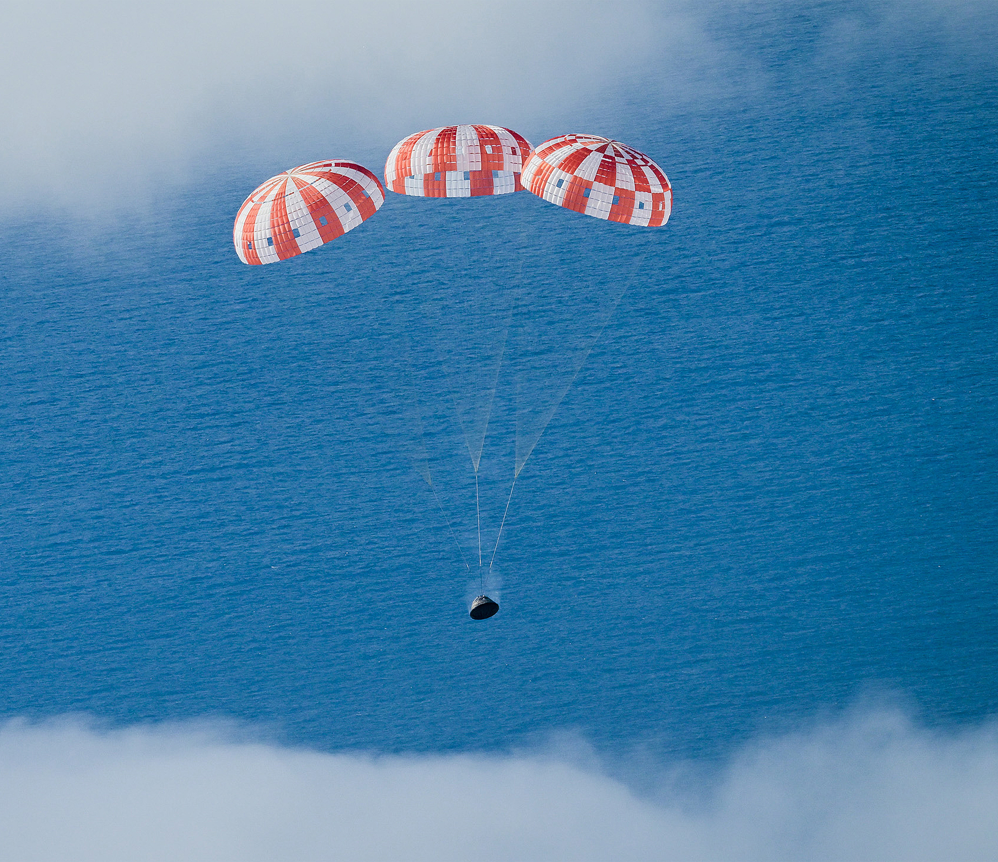 Artemis Space Capsule Under Three Large Parachutes, Dropping Towards Ocean with Clouds Behind, adapted from nasa.gov image